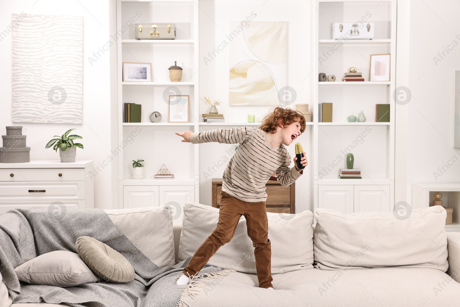 Photo of Little boy with microphone singing on sofa at home