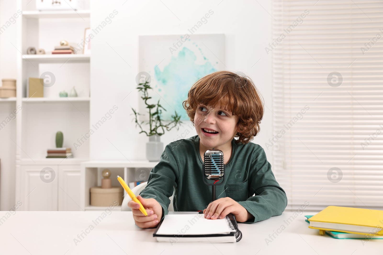 Photo of Little boy with microphone at white table indoors