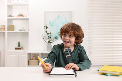 Photo of Little boy with microphone at white table indoors