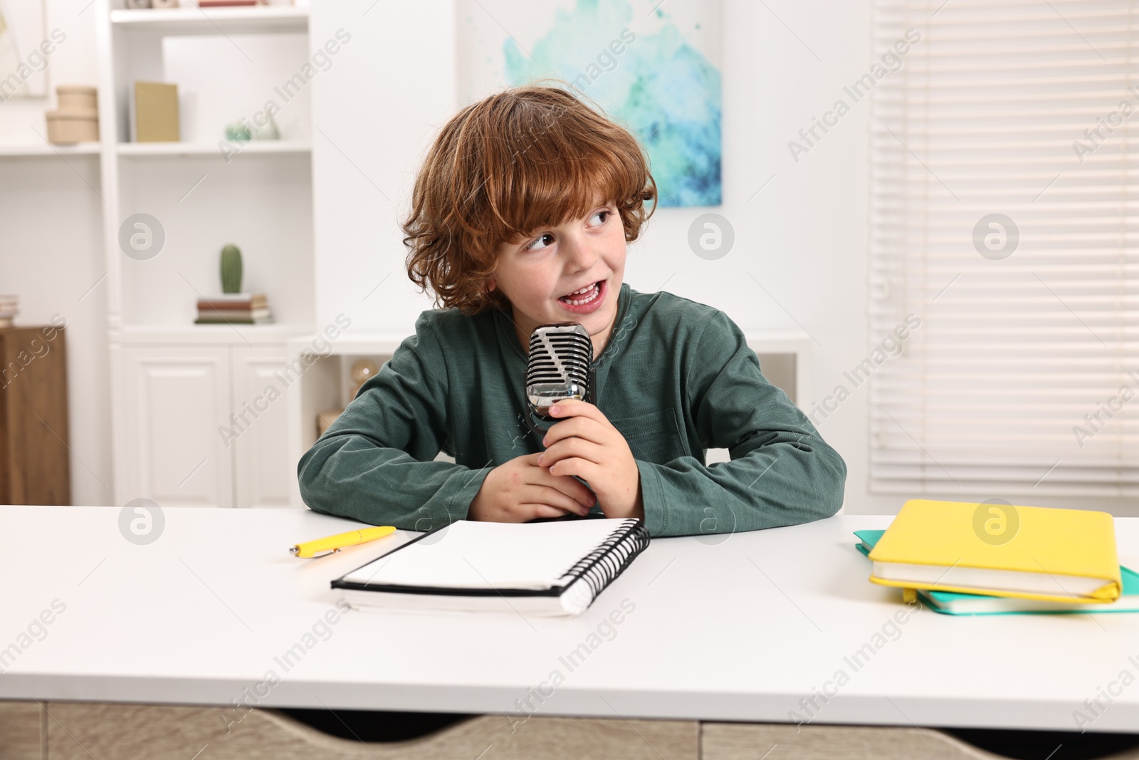 Photo of Little boy with microphone at white table indoors