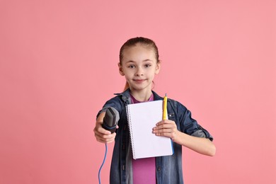 Little girl with microphone and notebook on pink background