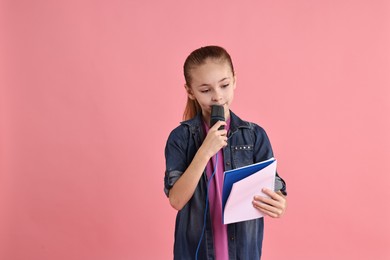 Photo of Little girl with microphone and notebook on pink background