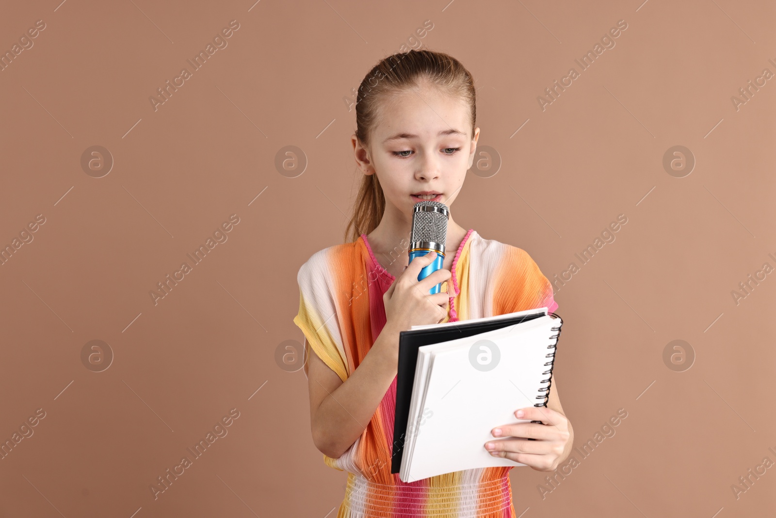 Photo of Little girl with microphone and notebook on light brown background