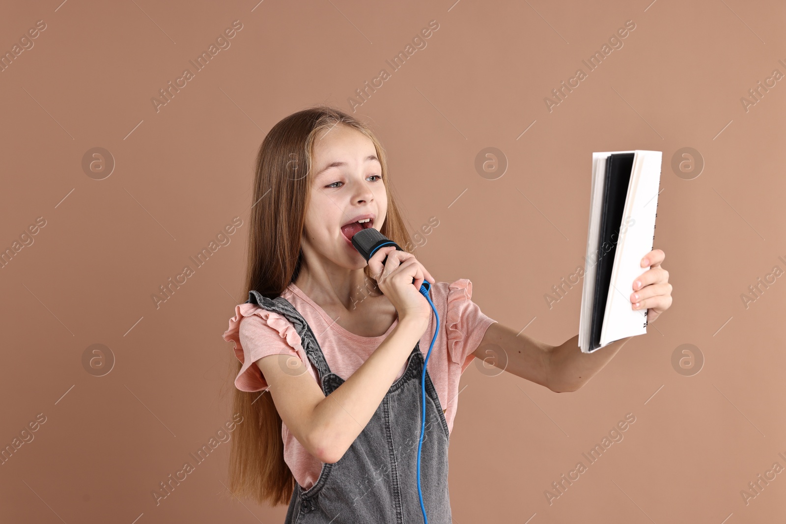 Photo of Little girl with microphone and notebook singing on light brown background