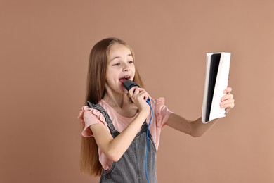 Photo of Little girl with microphone and notebook singing on light brown background