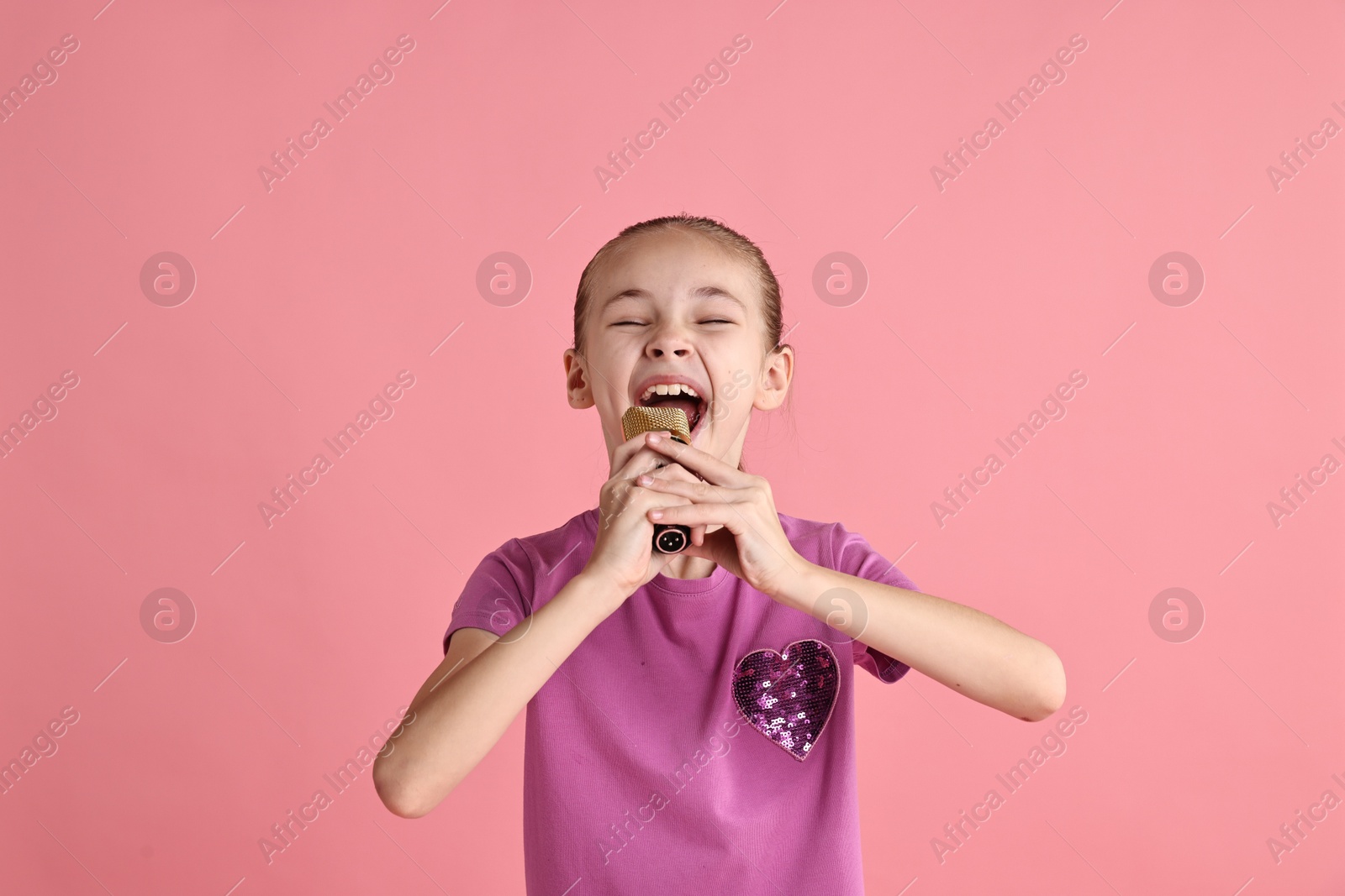 Photo of Little girl with microphone singing on pink background