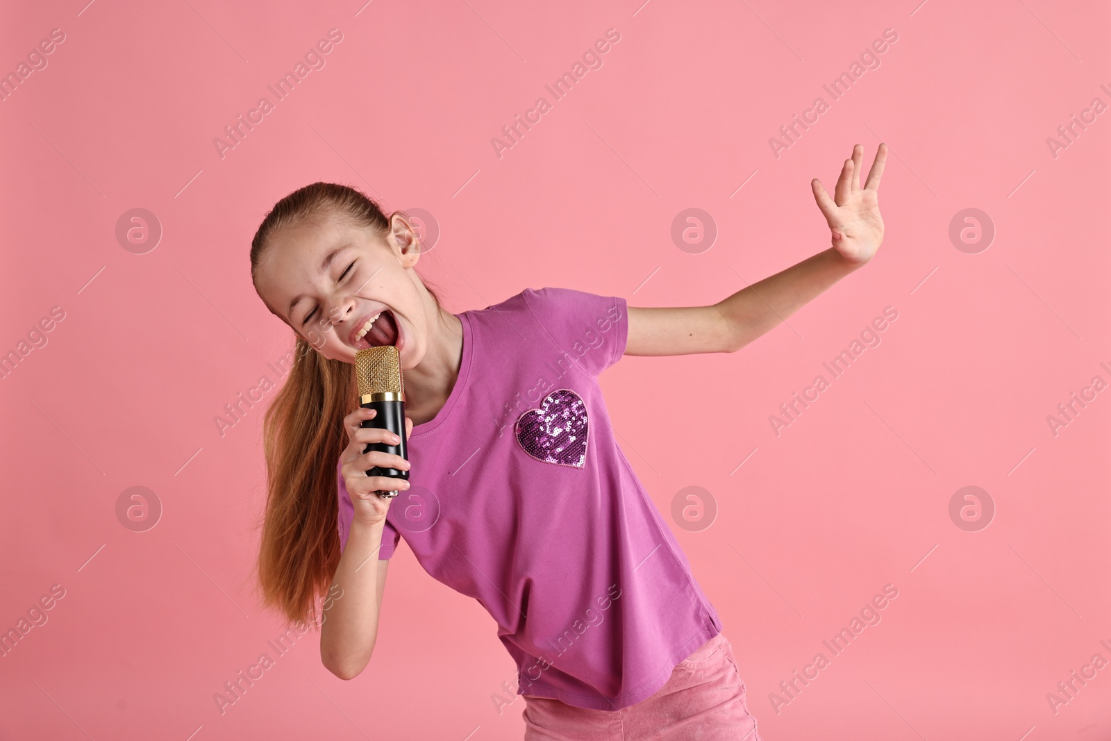 Photo of Little girl with microphone singing on pink background