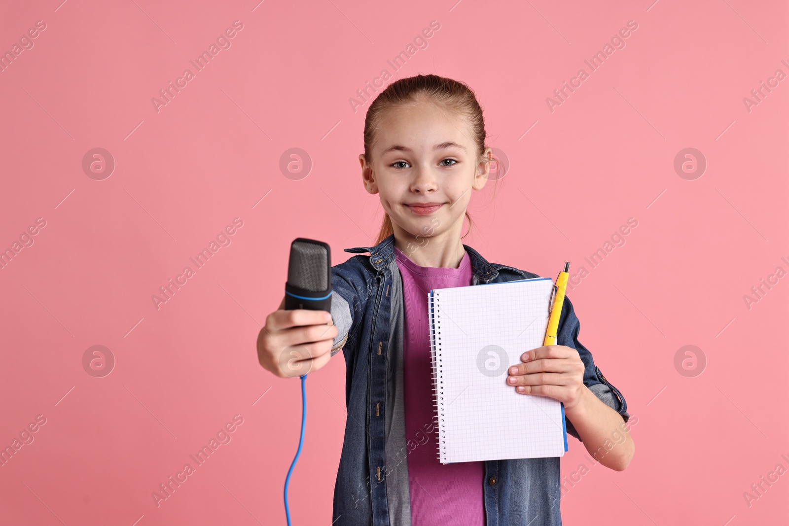 Photo of Little girl with microphone and notebook on pink background