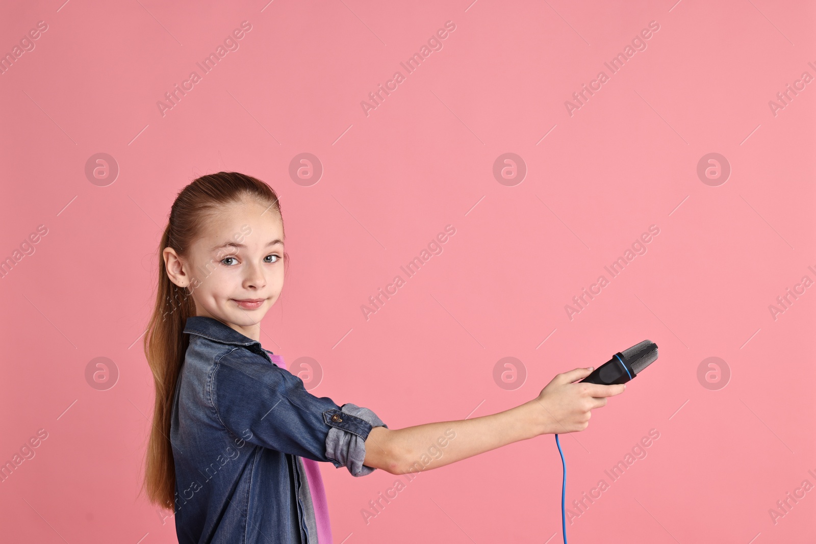 Photo of Little girl with microphone on pink background, space for text