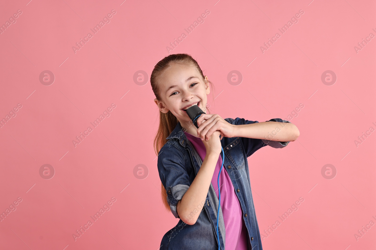 Photo of Little girl with microphone singing on pink background