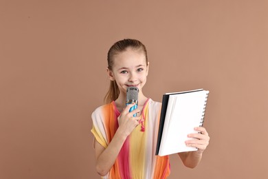 Photo of Little girl with microphone and notebook on light brown background