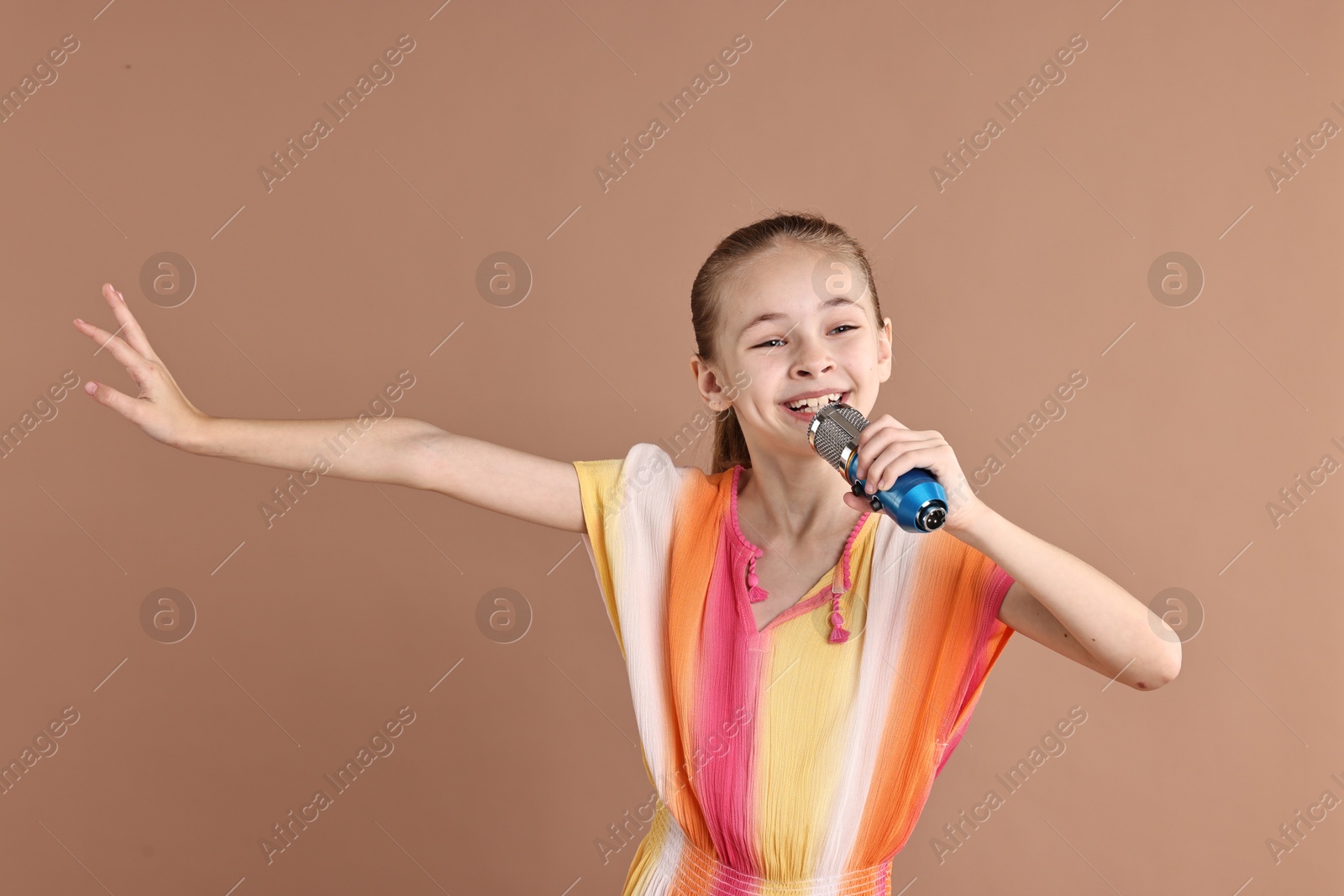 Photo of Little girl with microphone singing on light brown background