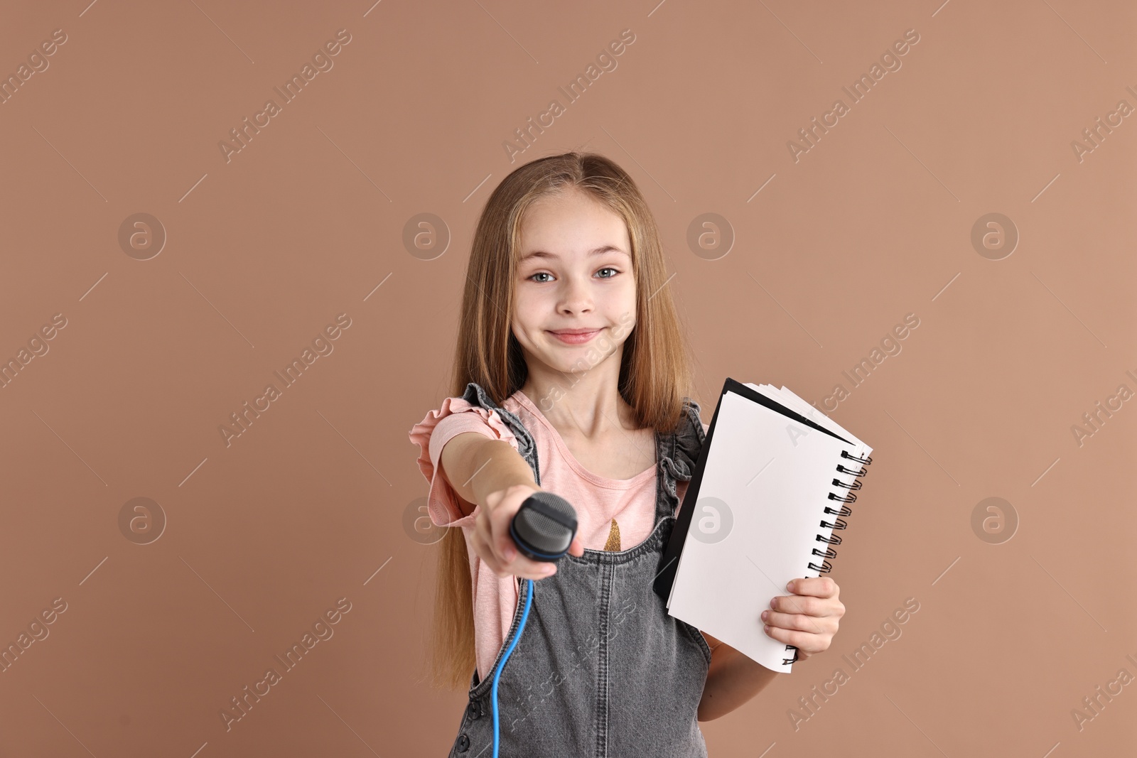 Photo of Little girl with microphone and notebook on light brown background