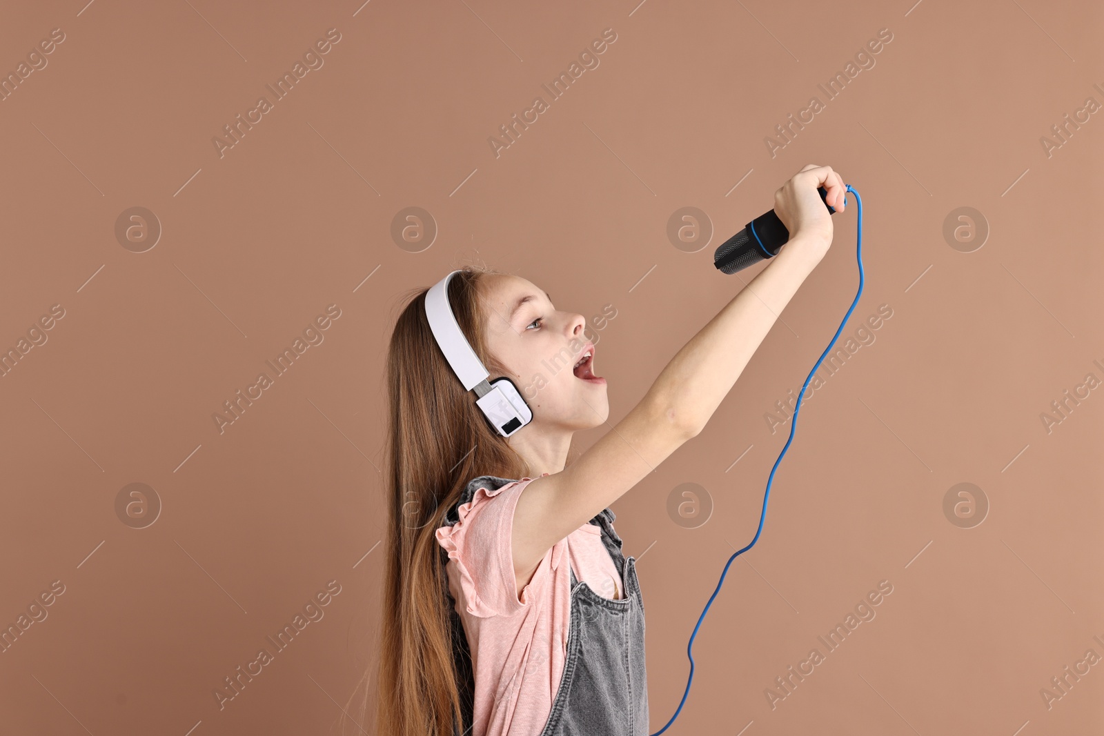 Photo of Little girl with microphone and headphones singing on light brown background