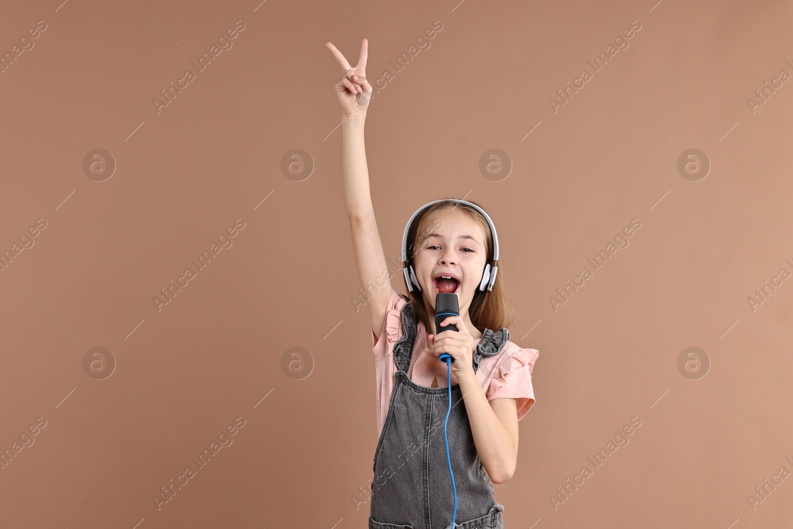 Photo of Little girl with microphone and headphones singing on light brown background