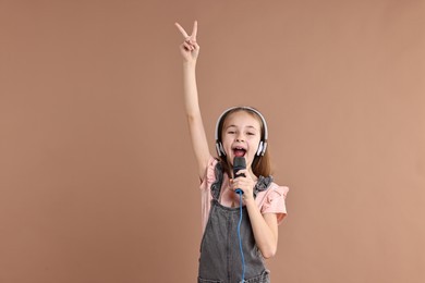 Photo of Little girl with microphone and headphones singing on light brown background