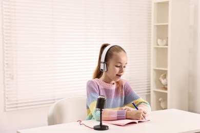 Photo of Little girl with microphone and headphones at white table indoors