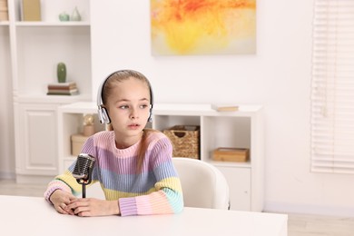 Photo of Little girl with microphone and headphones at white table indoors, space for text