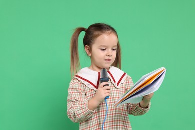 Photo of Cute girl with microphone and notebook on green background