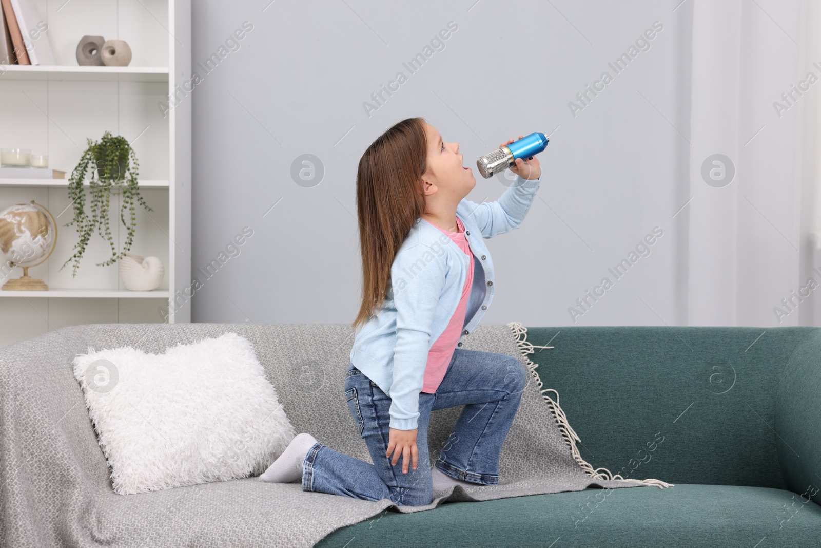 Photo of Cute girl with microphone singing on sofa at home