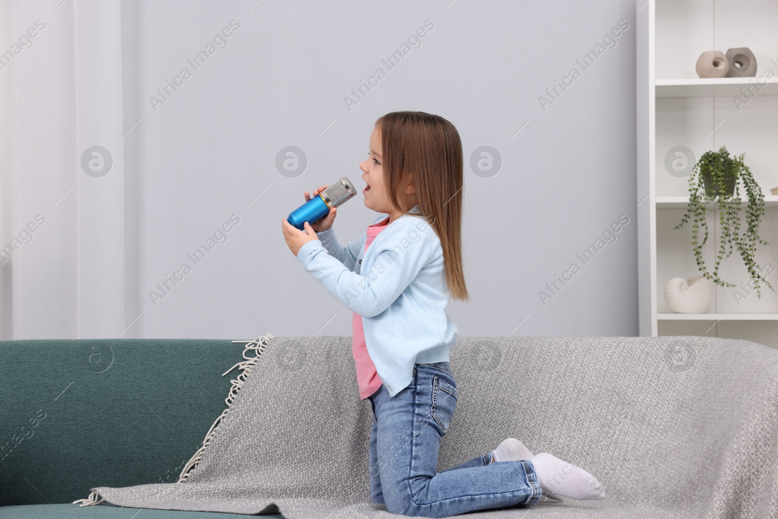 Photo of Cute girl with microphone singing on sofa at home