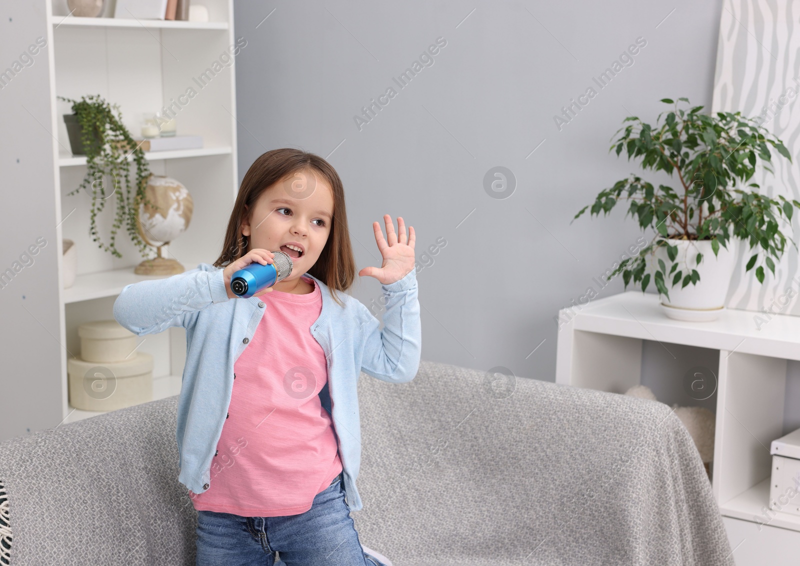 Photo of Cute girl with microphone singing on sofa at home