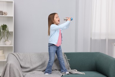 Photo of Cute girl with microphone singing on sofa at home