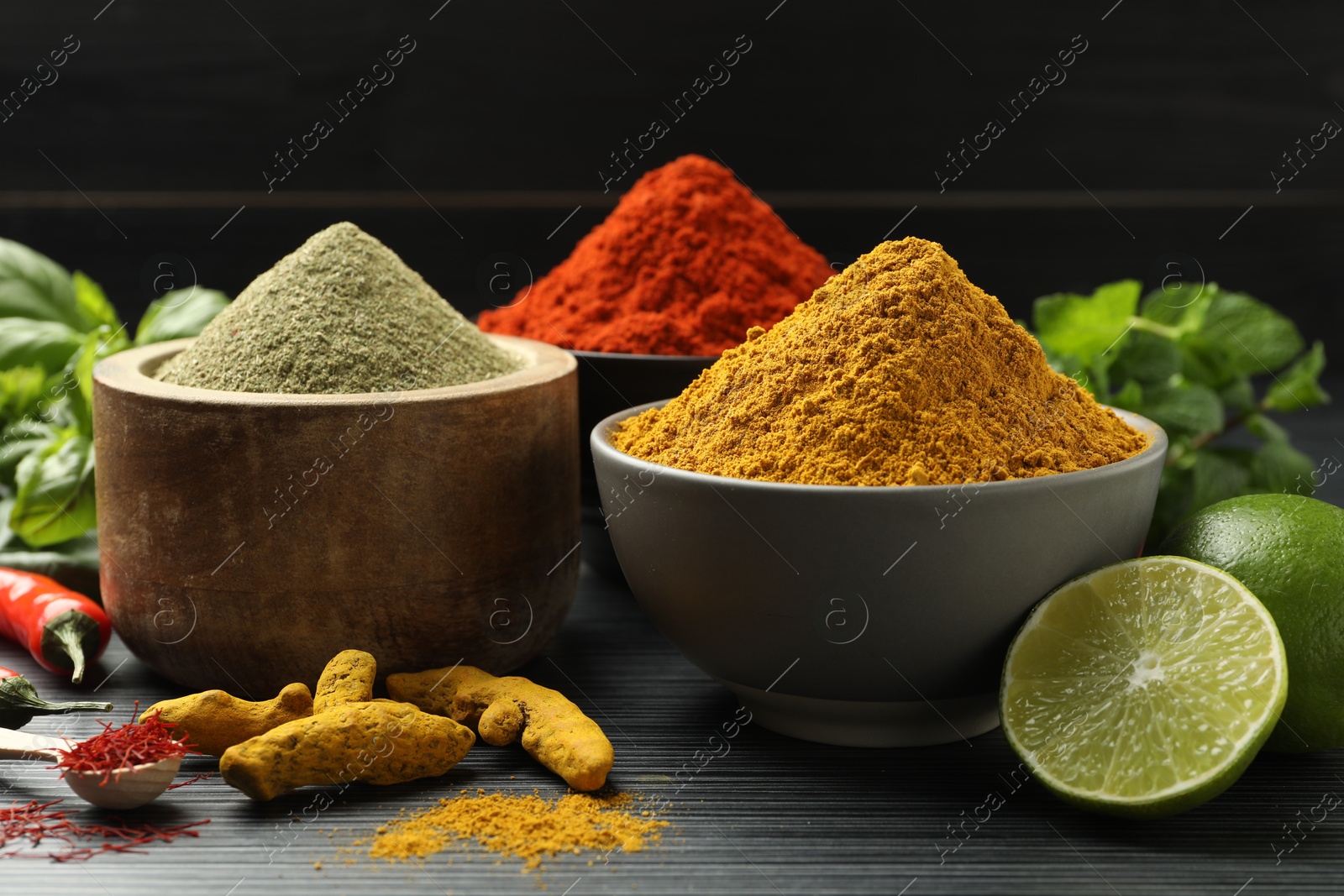 Photo of Different aromatic spices, lime and herbs on black background, closeup