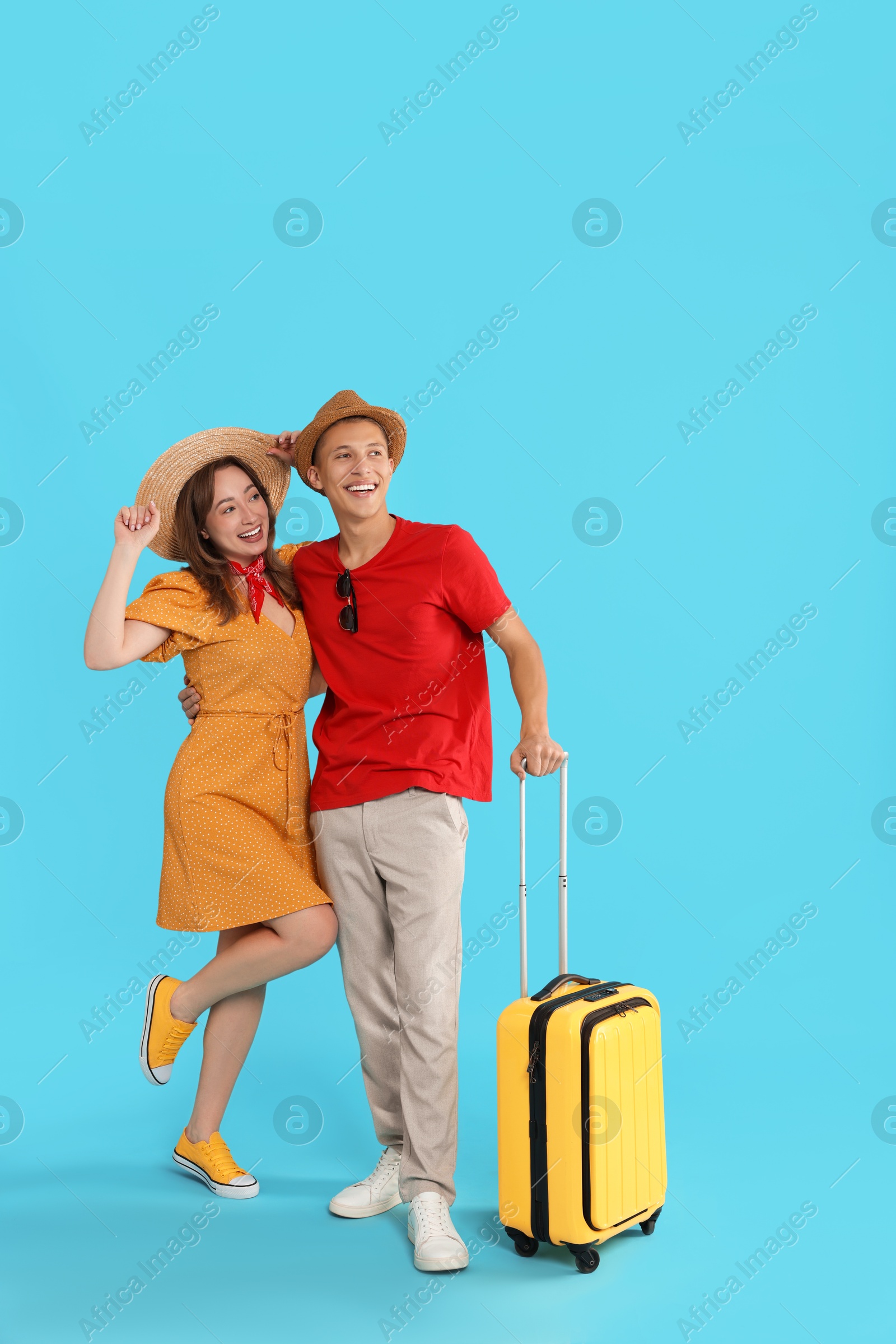 Photo of Happy travellers with suitcase on light blue background