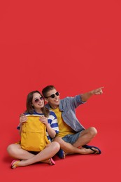 Photo of Happy travellers with backpack looking at something on red background, space for text