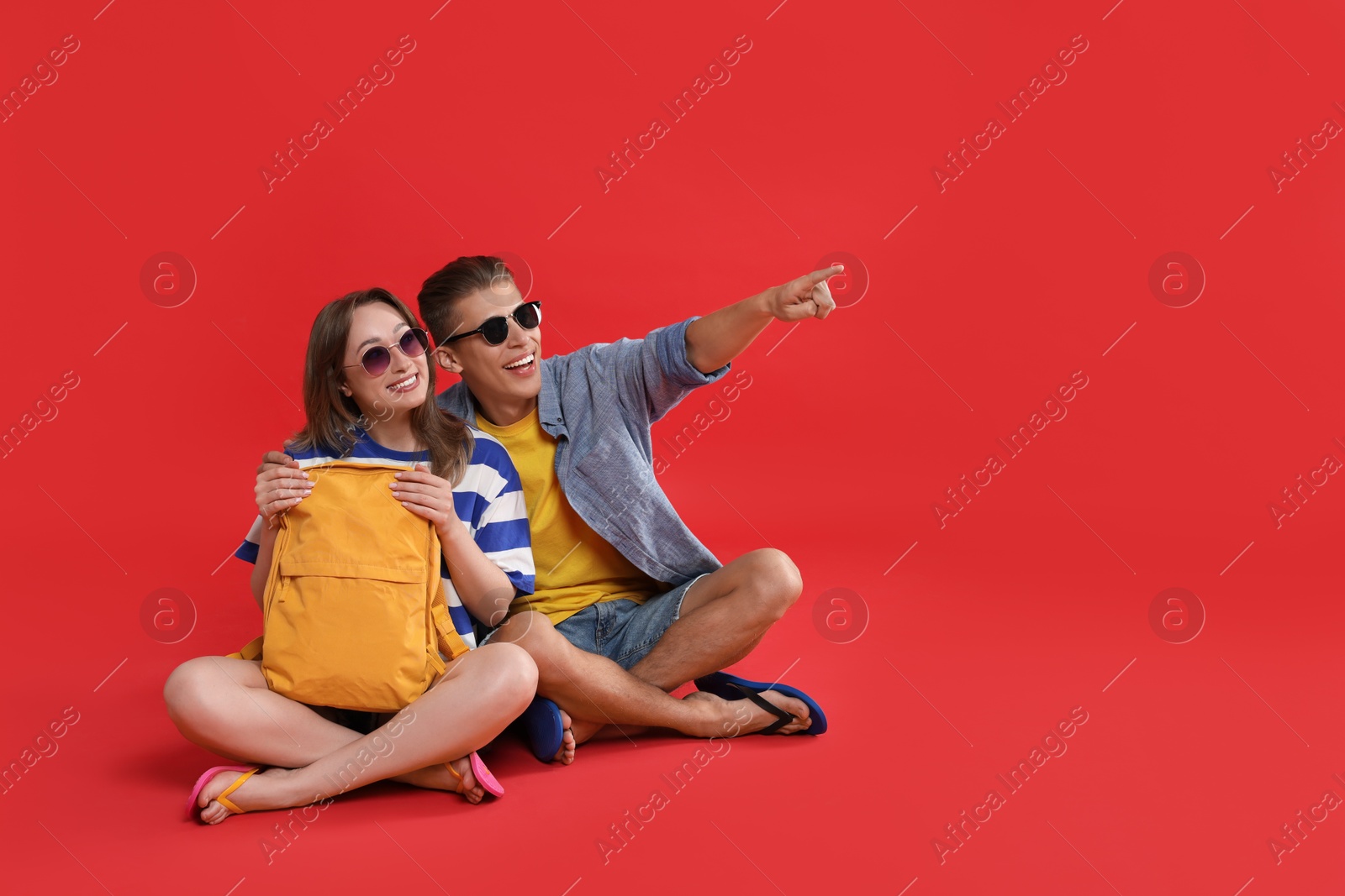 Photo of Happy travellers with backpack looking at something on red background, space for text