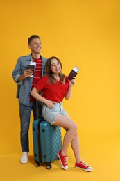 Photo of Happy travellers with suitcase, passports and tickets on yellow background