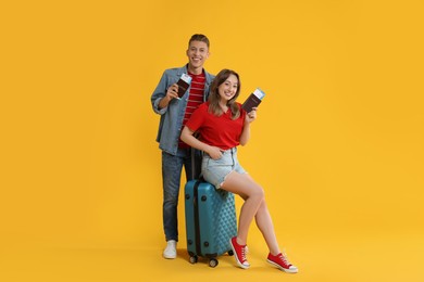 Photo of Happy travellers with suitcase, passports and tickets on yellow background