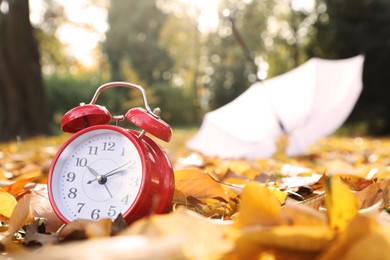 Photo of Alarm clock and white umbrella on dry leaves outdoors, closeup. Space for text