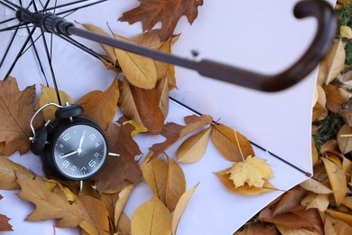 Photo of Alarm clock and white umbrella on dry leaves, above view