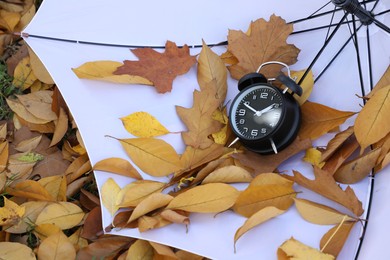 Photo of Alarm clock and white umbrella on dry leaves, above view