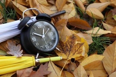 Photo of Alarm clock and umbrellas on dry leaves outdoors, closeup. Space for text