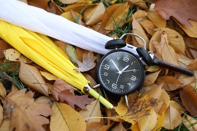 Photo of Alarm clock and umbrellas on dry leaves outdoors, top view