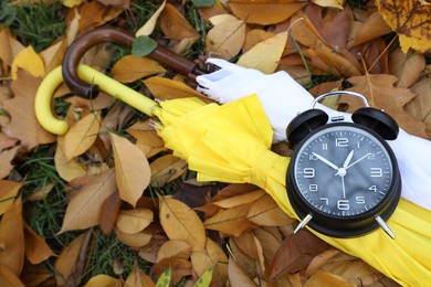 Photo of Alarm clock and umbrellas on dry leaves outdoors, above view. Space for text