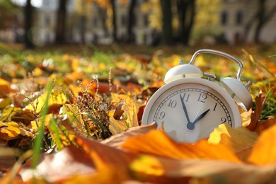 Photo of Alarm clock on dry leaves in park, closeup. Space for text