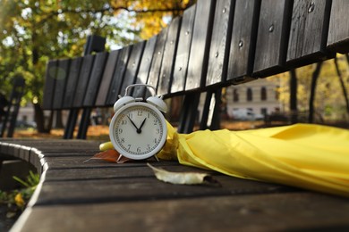 Photo of Alarm clock and yellow umbrella on wooden bench outdoors