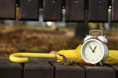 Photo of Alarm clock and yellow umbrella on wooden bench outdoors