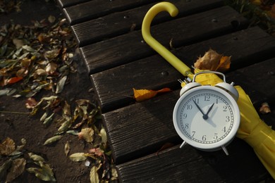 Photo of Alarm clock and yellow umbrella on wooden bench outdoors. Space for text