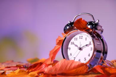 Photo of Alarm clock and dry leaves on blurred background, closeup. Space for text