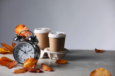 Photo of Alarm clock, dry leaves and cups of coffee on light grey background, space for text