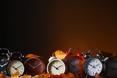 Photo of Alarm clocks and dry leaves on brown background, space for text