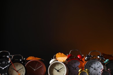 Photo of Alarm clocks and dry leaves on brown background, space for text