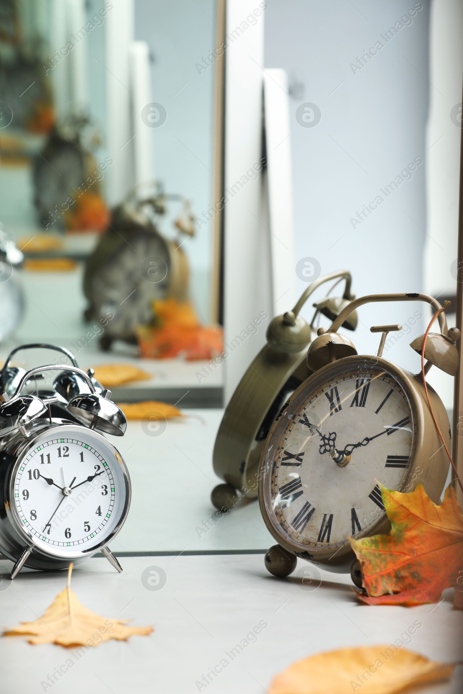 Photo of Alarm clocks and dry leaves near mirror on white table