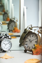 Photo of Alarm clocks and dry leaves near mirror on white table