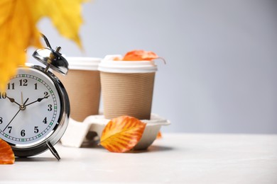 Photo of Alarm clock, dry leaves and cups of coffee on light grey background, closeup. Space for text